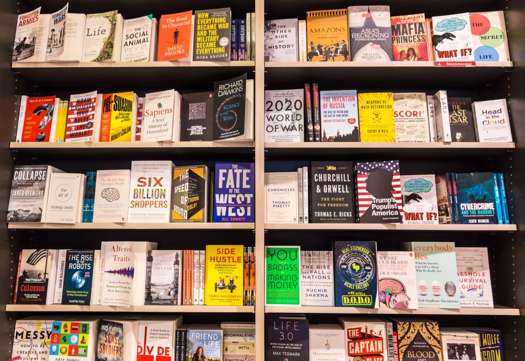 Bookshelves filled with a variety of books, all facing outward. Titles include "Sapiens," "2020 World of War," "Six Billion Shoppers," and "Everybody Lies." The books are arranged by genre and cover various topics like history, science, business, and self-help. A Beta Reading Service is also available for aspiring authors. BookSelf Book Cover Design & Premade Book Covers