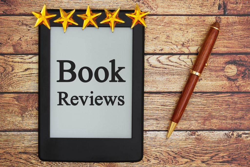 An e-reader displaying "Book Reviews" on the screen sits on a wooden surface. Above the e-reader, five golden stars form a row, indicating a five-star rating. To the right of the e-reader, there is a brown and gold pen placed horizontally—a signature touch by BookSelf UK’s premier book reviews service. BookSelf Book Cover Design & Premade Book Covers